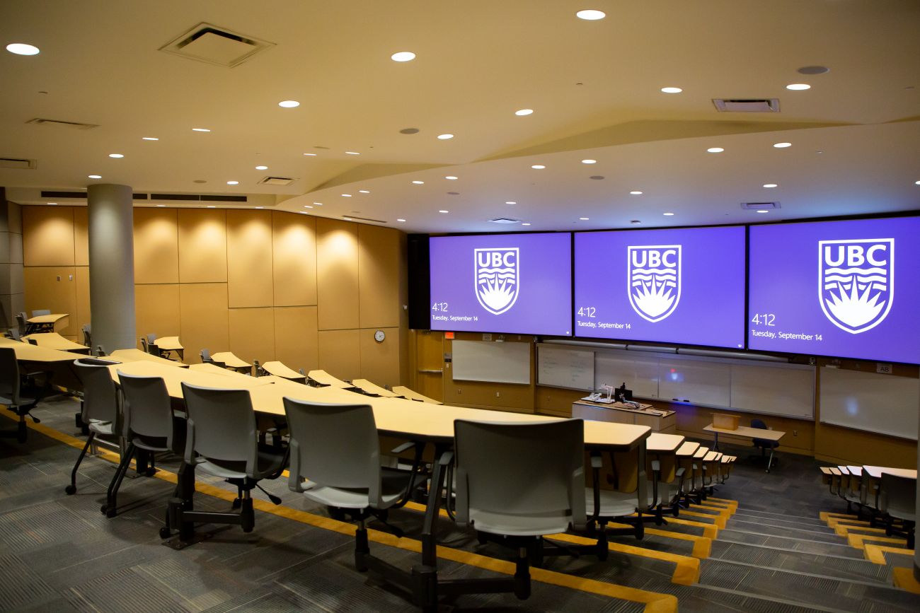 A lecture hall with the UBC logo projected on several monitors